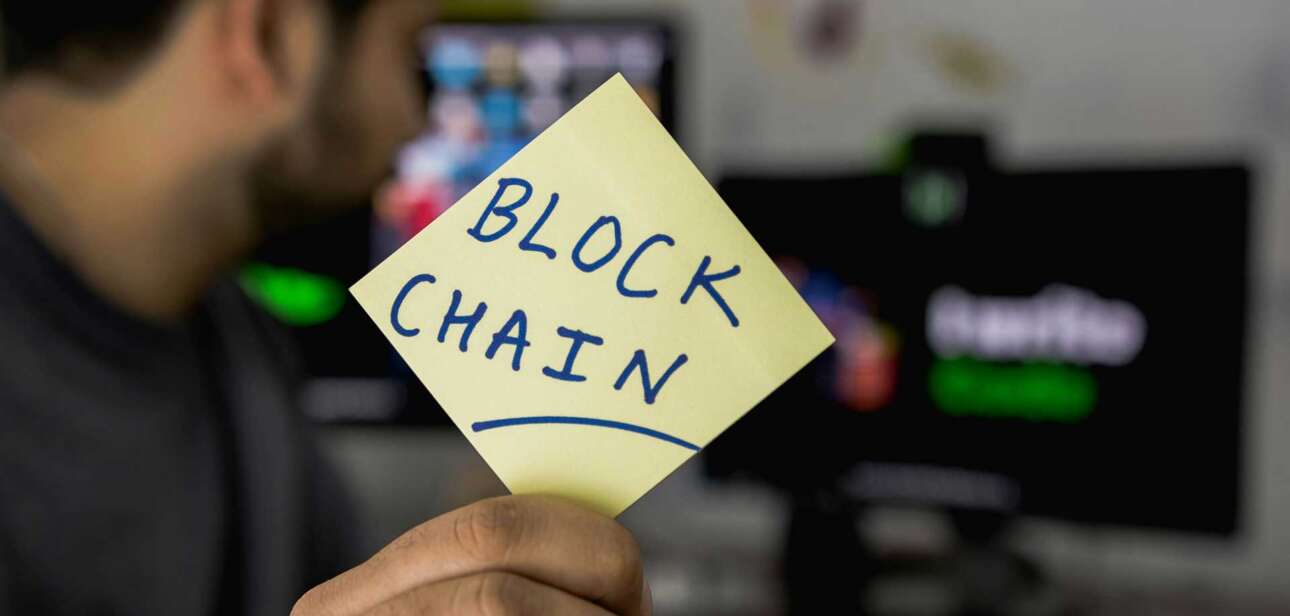 Man holding a post-it note with blockchin written on it