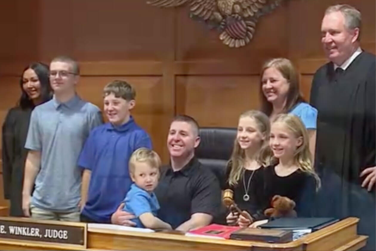 Group photo in a courtroom showing an adult couple with five children of various ages, standing with a judge in a black robe.