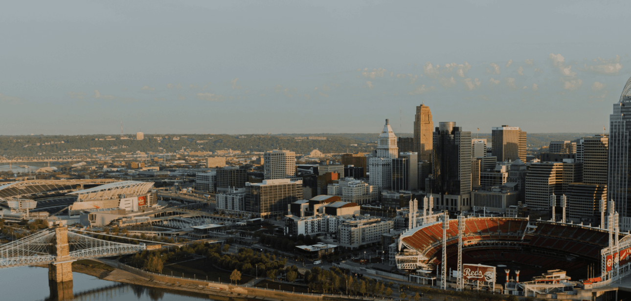 Aerial view of downtown Cincinnati, including Great American Ball Park and surrounding riverfront buildings at sunset that is covered in The Banks redevelopment.