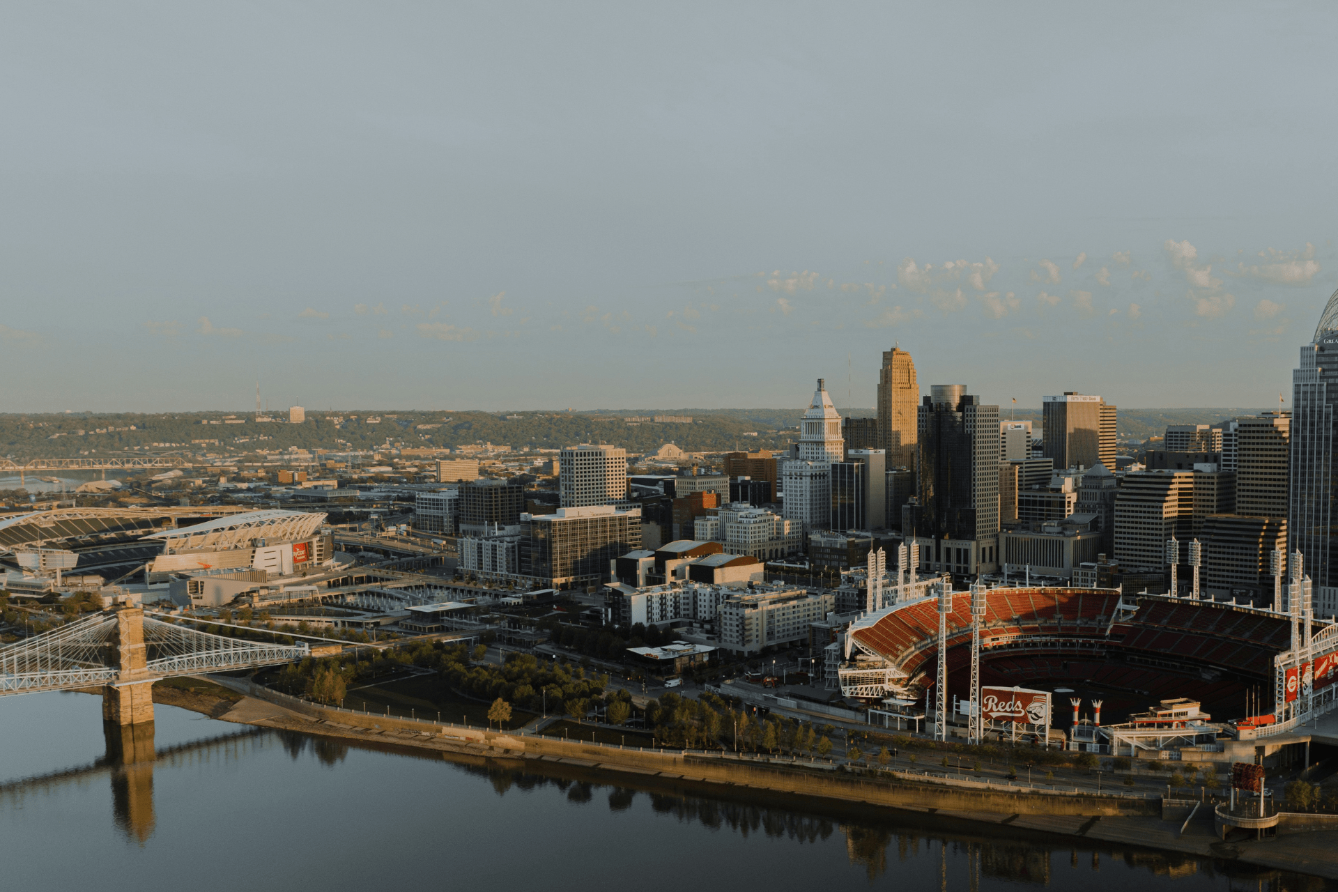 Aerial view of downtown Cincinnati, including Great American Ball Park and surrounding riverfront buildings at sunset that is covered in The Banks redevelopment.