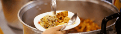 A volunteer ladles food into a bowl at a community kitchen, preparing meals for people facing food insecurity.