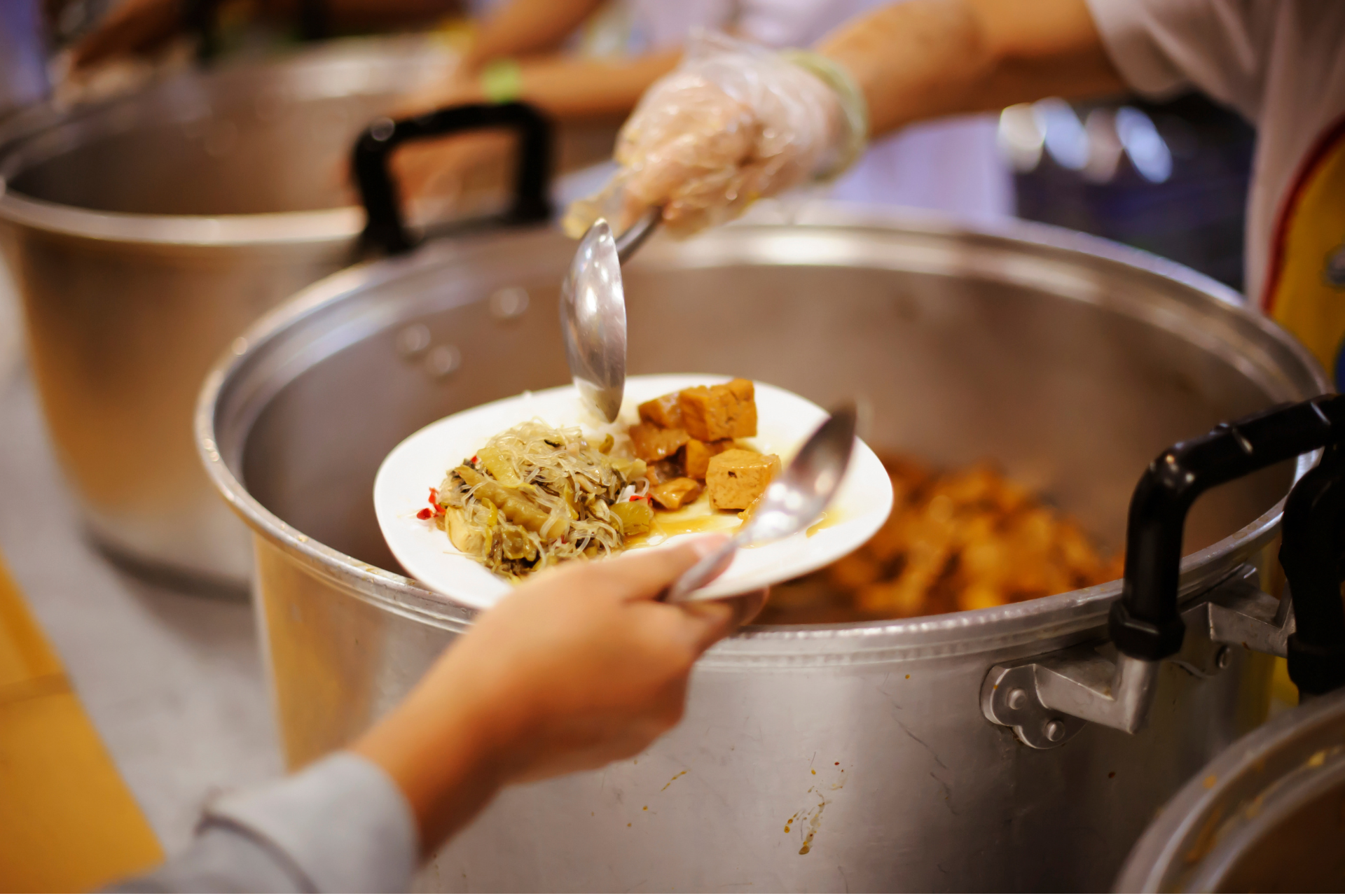 A volunteer ladles food into a bowl at a community kitchen, preparing meals for people facing food insecurity.