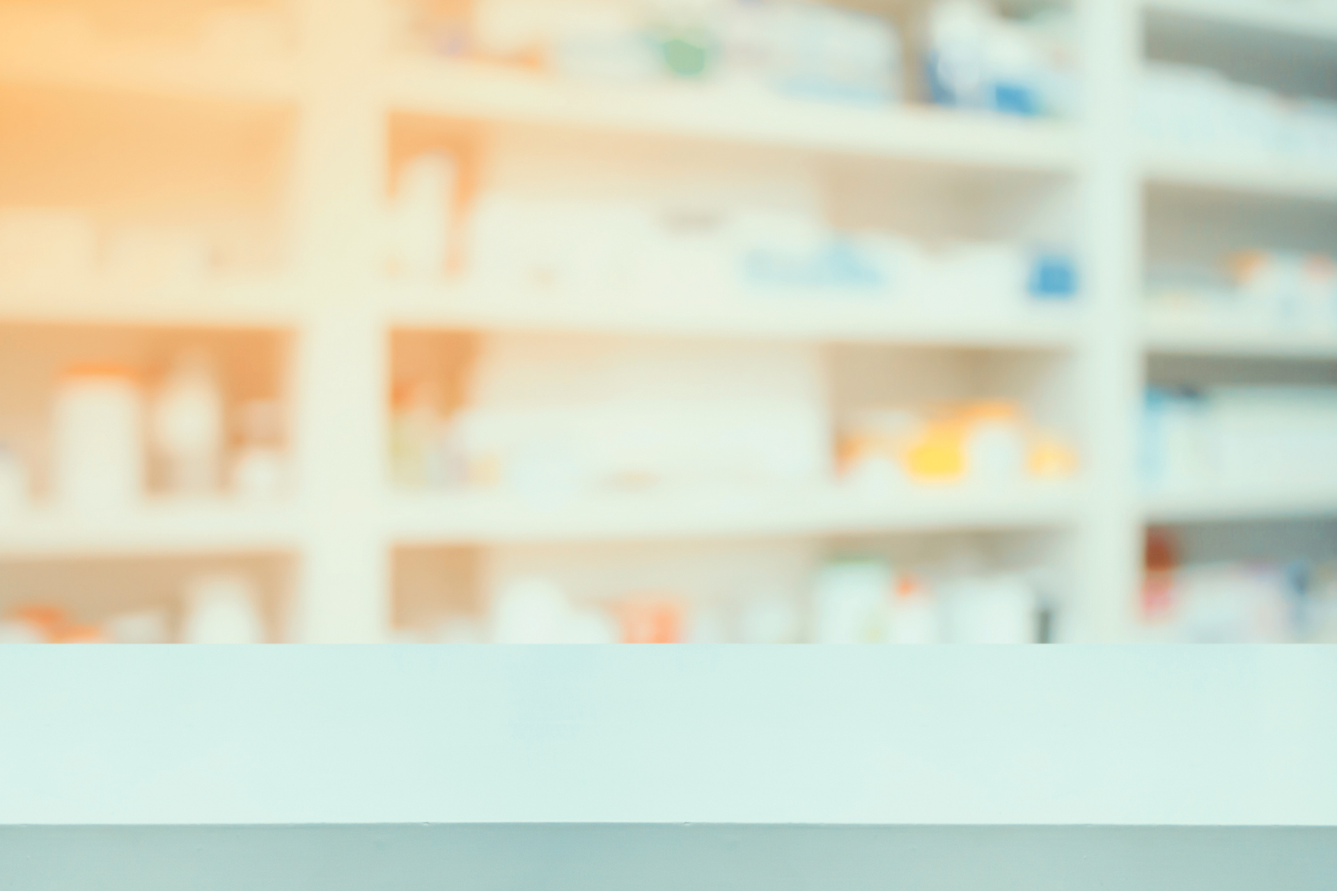 Blurred image of a pharmacy counter with prescription bottles on shelves in the background.