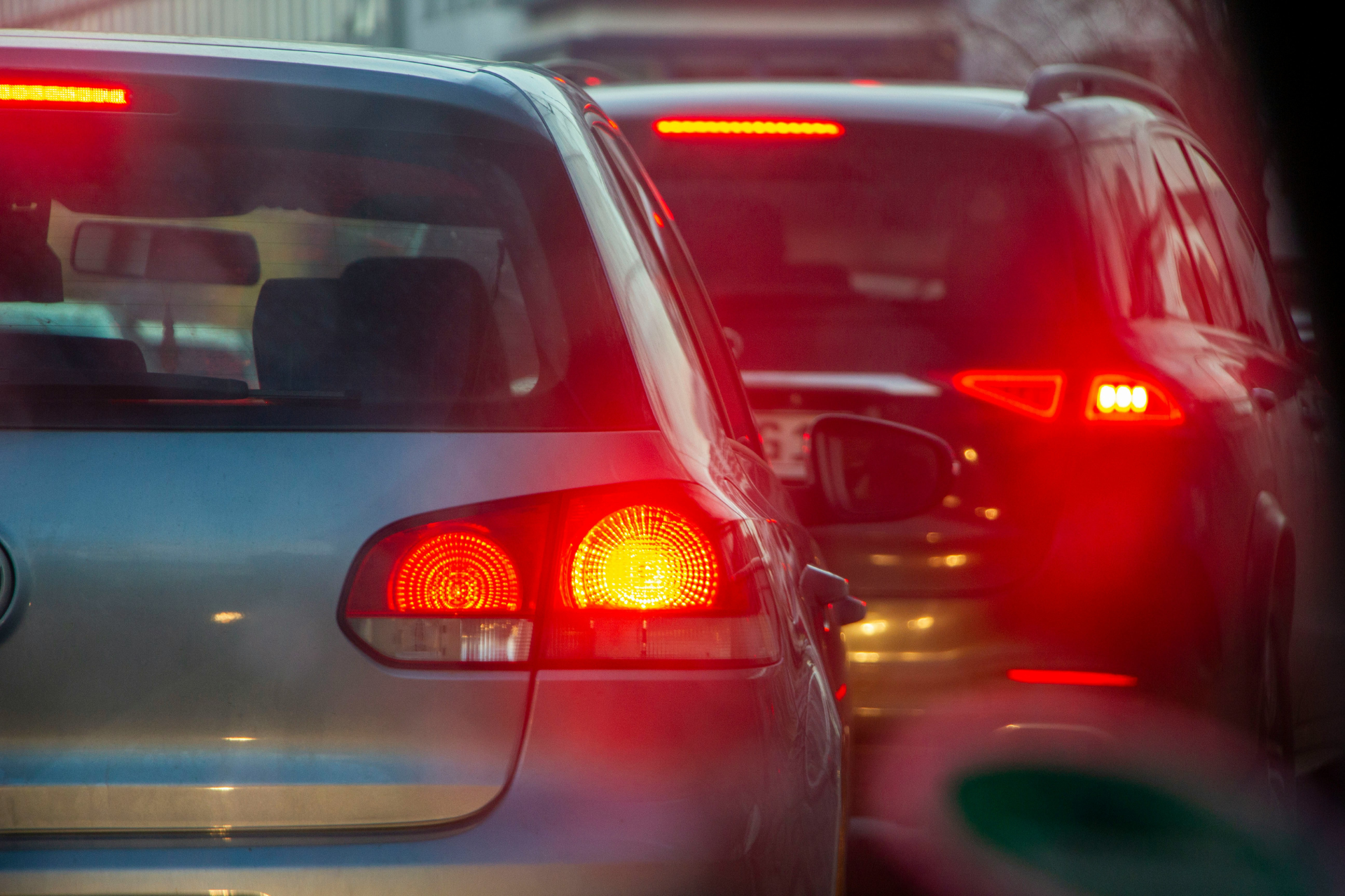 Cars stopped in heavy traffic with red brake lights glowing on a busy roadway.