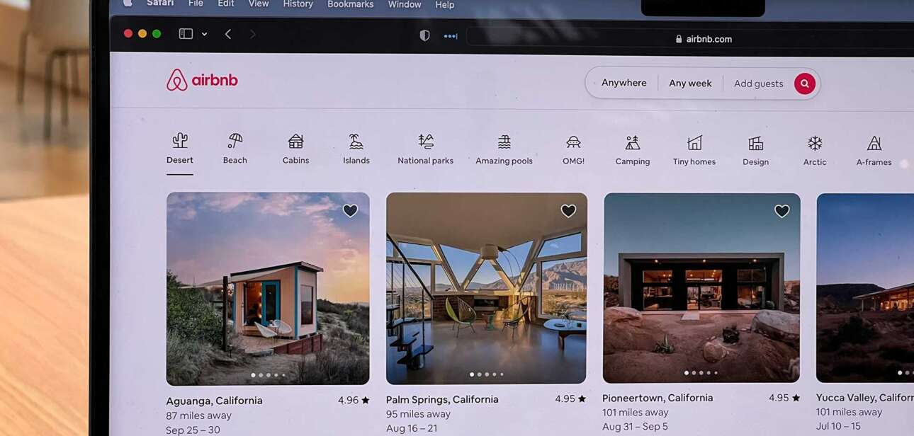 A laptop screen displaying an Airbnb-style short-term rental listings interface, showing multiple rental options in a grid view.