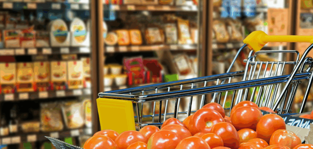 Grocery cart filled with fresh tomatoes in a supermarket produce aisle.
