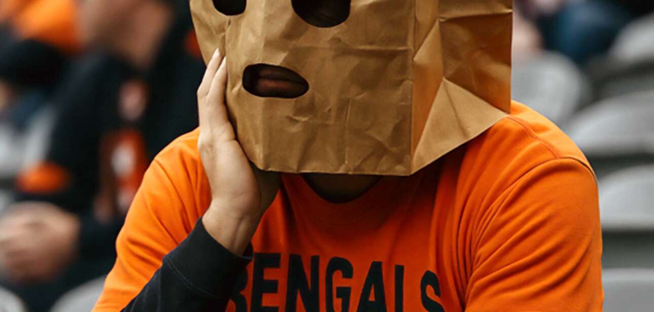 Dejected Cincinnati Bengals fan wearing a paper bag over their head after a loss, sitting in the stadium looking disappointed.