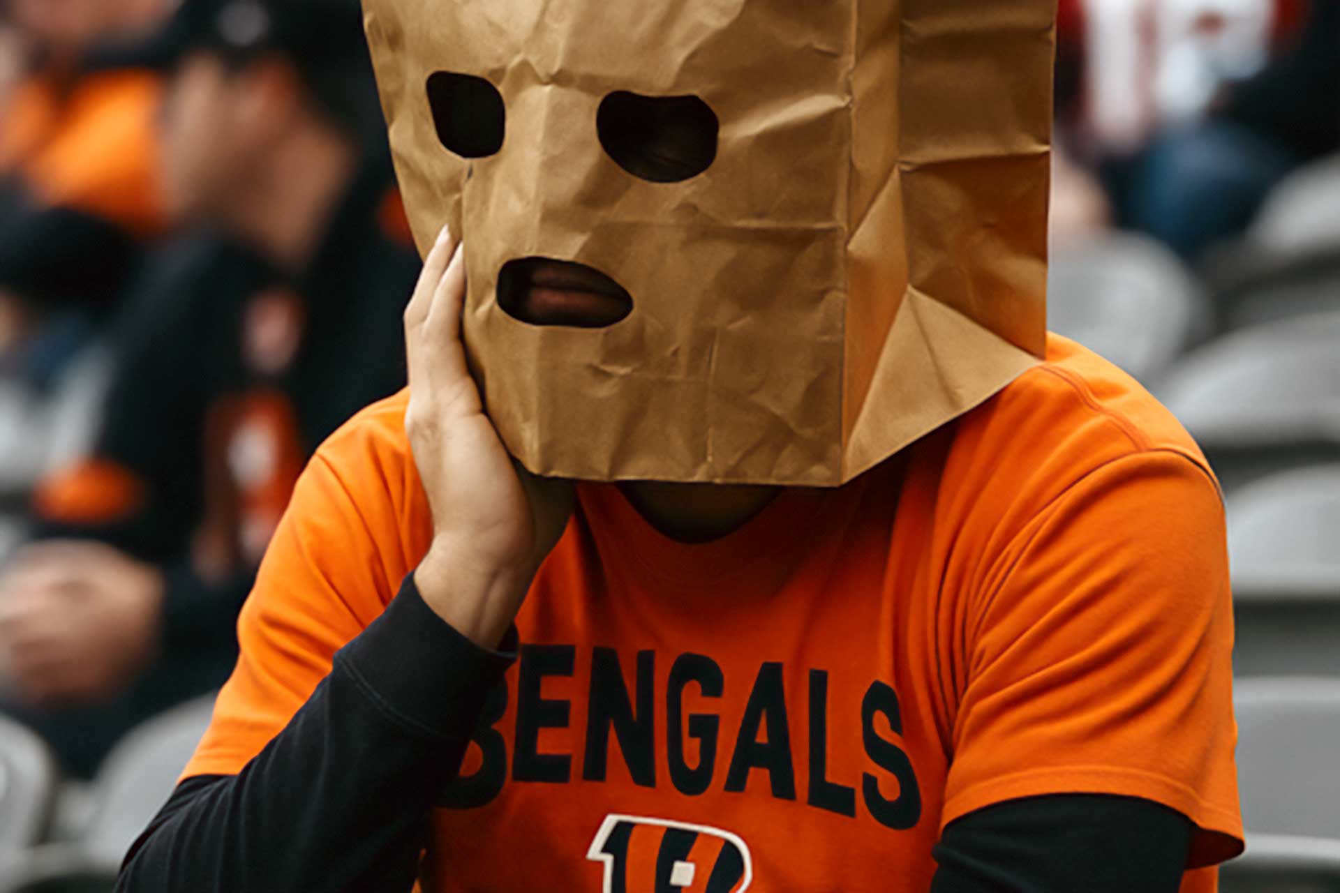 Dejected Cincinnati Bengals fan wearing a paper bag over their head after a loss, sitting in the stadium looking disappointed.