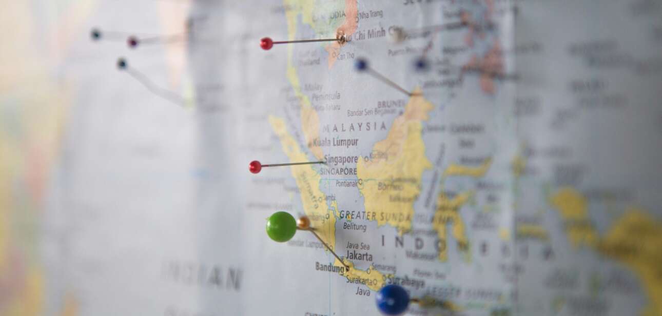 Illustrated world map with colorful push pins marking multiple travel destinations, representing a 2026 travel bucket list with weekend getaways, mid-length trips, and long adventures.