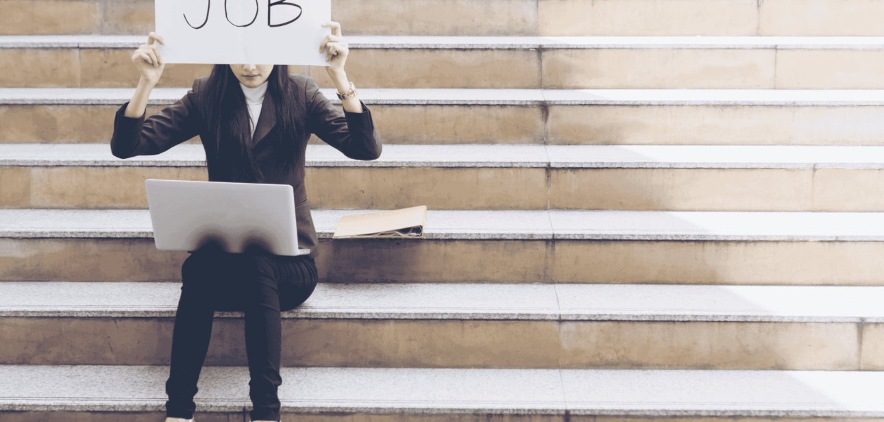 Job seeker sitting on steps holding a sign, illustrating the rising US unemployment rate in November 2025.