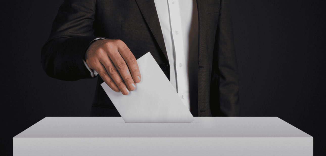 Close-up of a person in a suit casting a vote into a ballot box, representing Ohio mail-in ballot deadlines and grace period discussions.