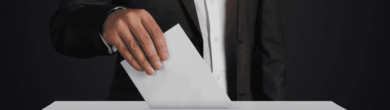 Close-up of a person in a suit casting a vote into a ballot box, representing Ohio mail-in ballot deadlines and grace period discussions.