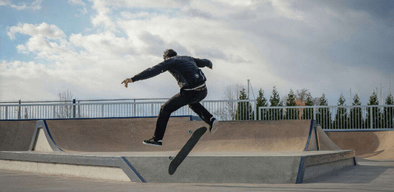Skateboarder performing a mid-air trick over a ramp that will be soon be seen at Camp Washington Skate Park in Cincinnati under a cloudy sky.