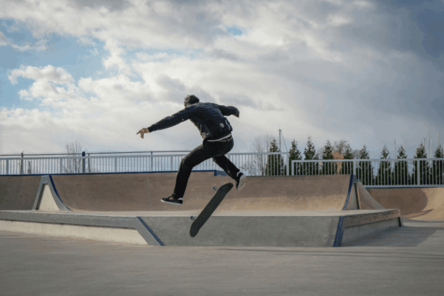 Skateboarder performing a mid-air trick over a ramp that will be soon be seen at Camp Washington Skate Park in Cincinnati under a cloudy sky.