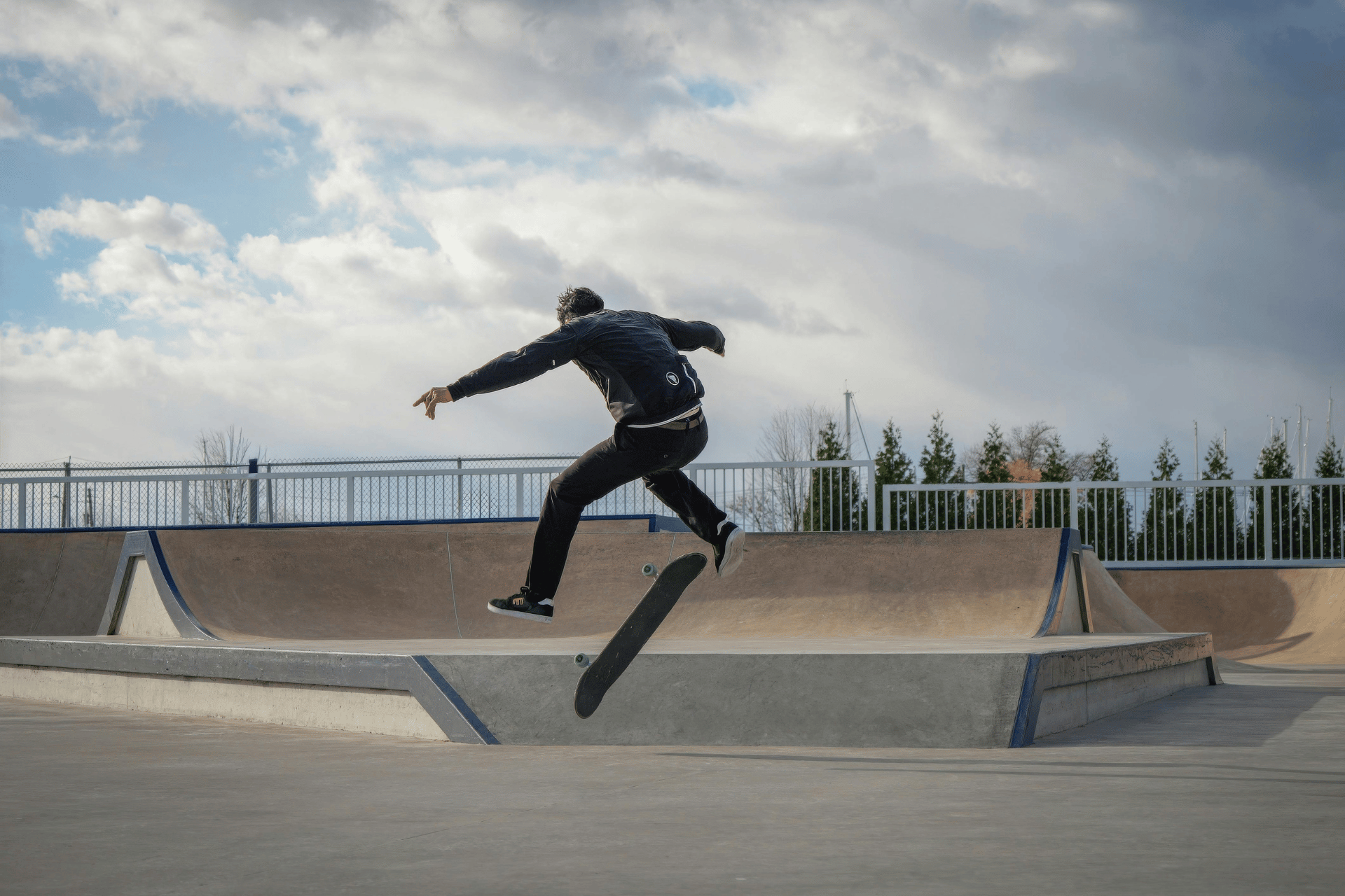 Skateboarder performing a mid-air trick over a ramp that will be soon be seen at Camp Washington Skate Park in Cincinnati under a cloudy sky.