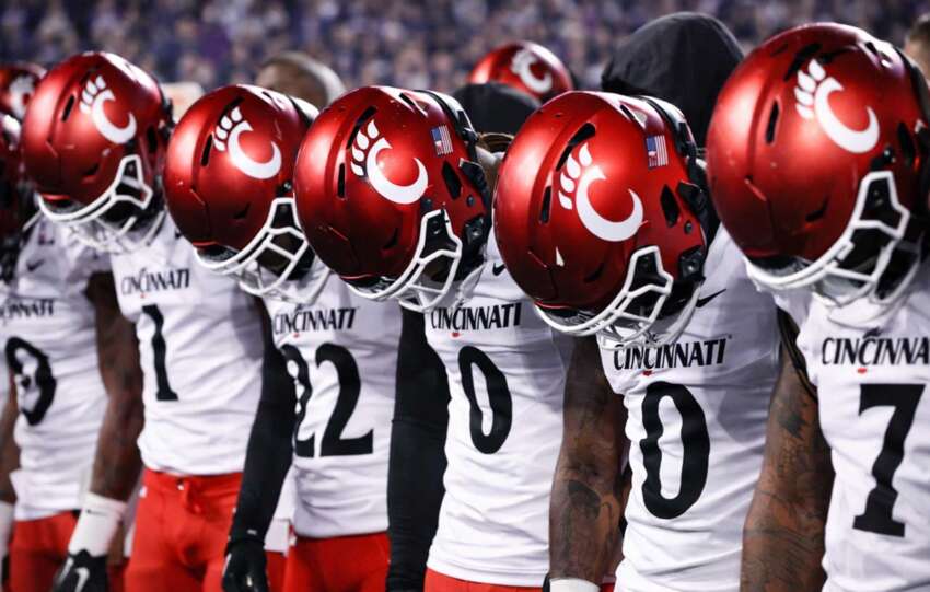 Cincinnati Bearcats football players stand on the sideline with heads down and helmets on during a night game