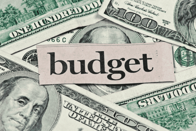 $100 bills spread out with a paper cutout reading "budget" placed on top.