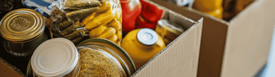 A collection of cardboard boxes filled with non-perishable food items, including canned goods and jars, prepared for distribution by a hunger-relief organization in Cincinnati.