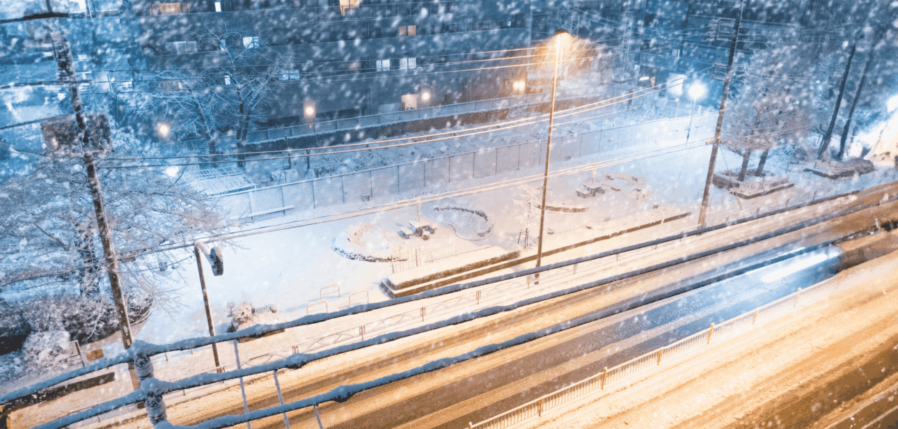 Stock image to represent a snow-covered street at night with streetlights and car light trails during a cold weather advisory in Cincinnati.
