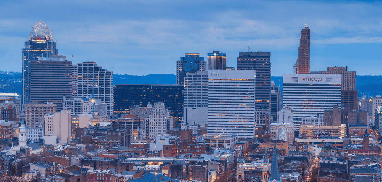 Cincinnati skyline at dusk, featuring the downtown buildings and the Ohio River.
