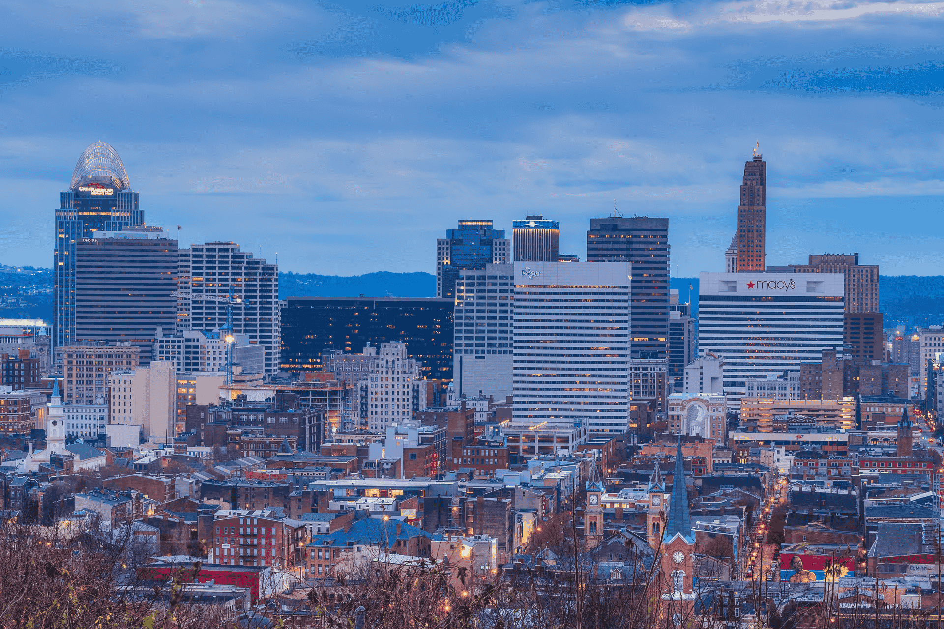 Cincinnati skyline at dusk, featuring the downtown buildings and the Ohio River.