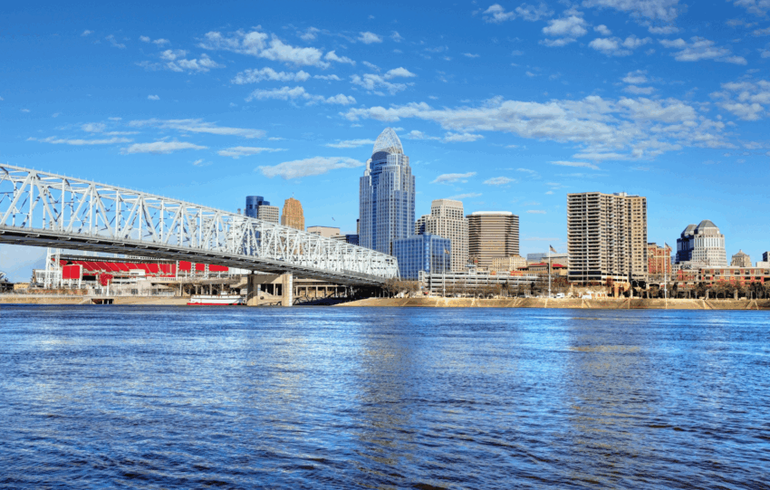 Cincinnati skyline and Ohio River waterfront with downtown skyscrapers and bridge during the day.