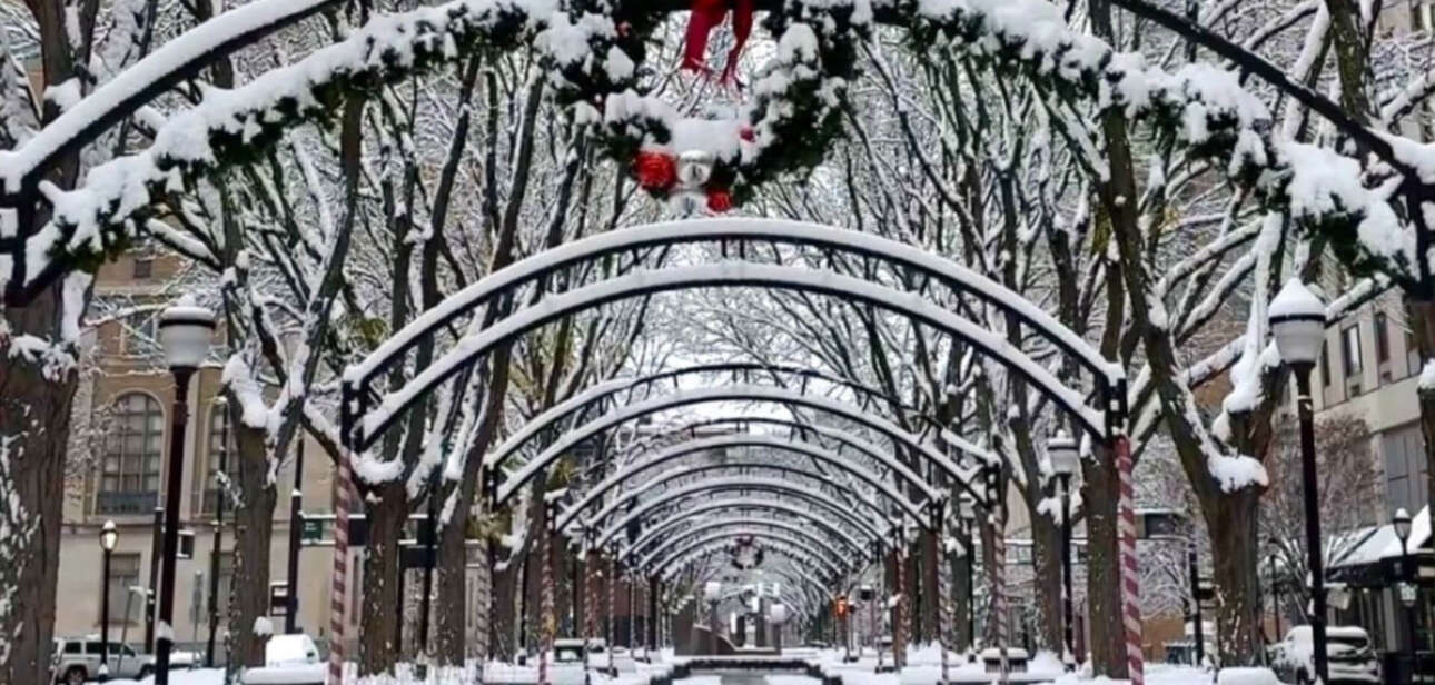 Snow covered pedestrian walkway in Cincinnati featuring arched trellises with holiday wreaths and snow dusted benches.