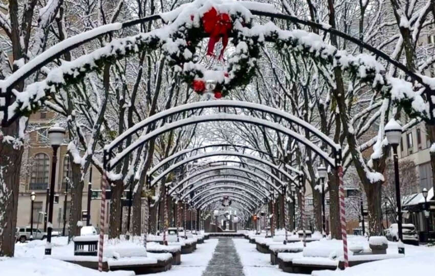 Snow covered pedestrian walkway in Cincinnati featuring arched trellises with holiday wreaths and snow dusted benches.