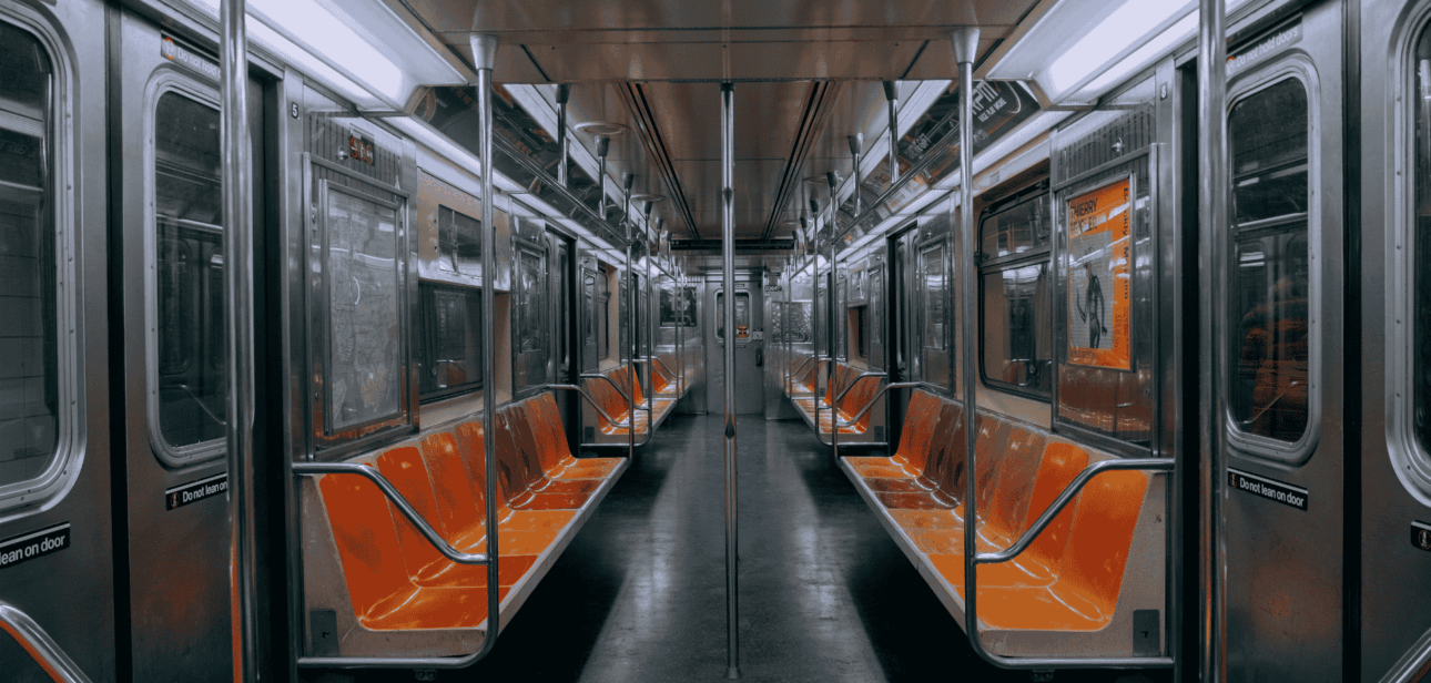Interior view of an empty subway car featuring orange and black seats, stainless steel poles, and bright overhead lighting.