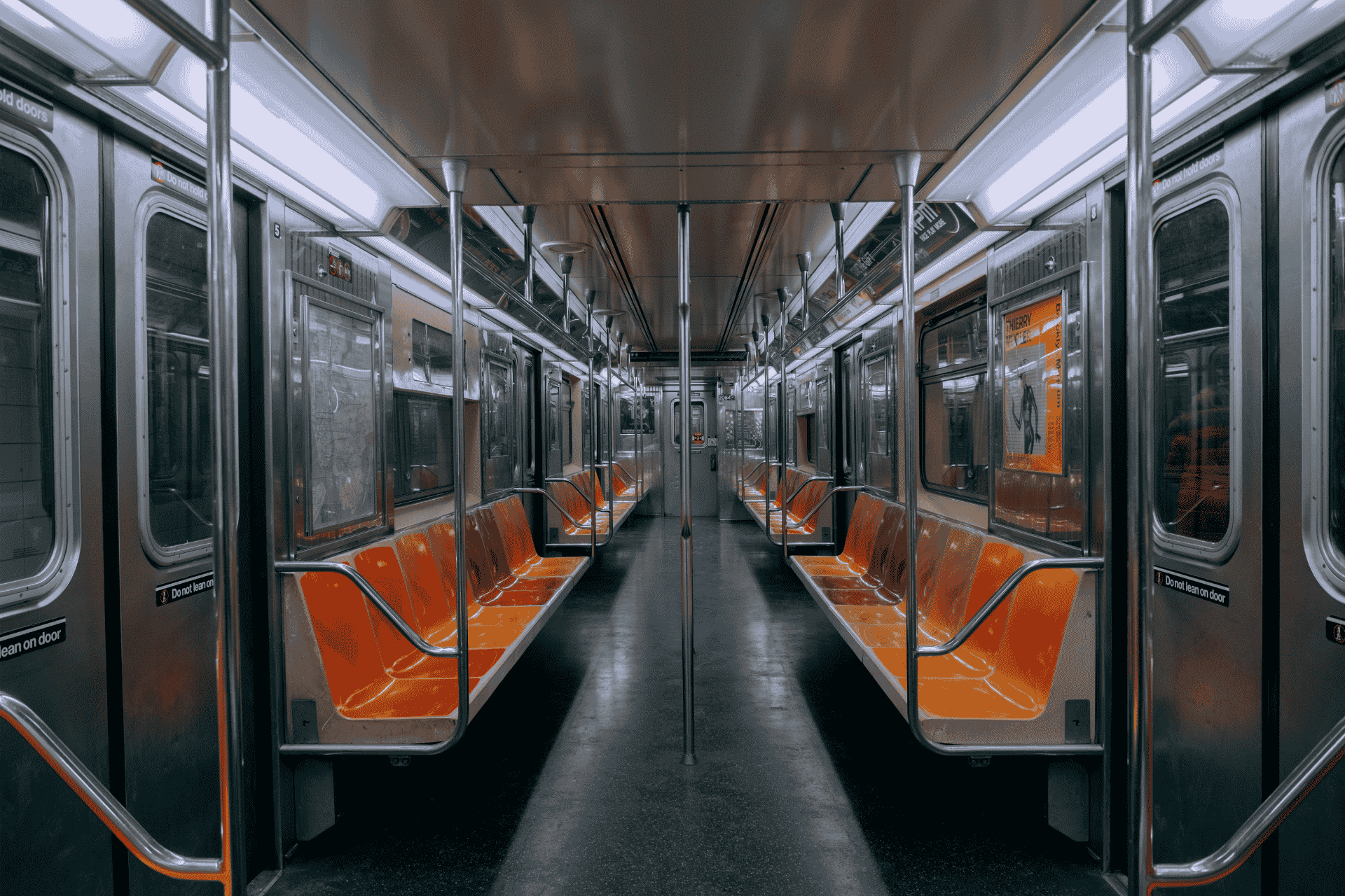 Interior view of an empty subway car featuring orange and black seats, stainless steel poles, and bright overhead lighting.