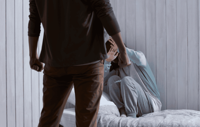 A person stands in the foreground while another individual cringes in a corner, illustrating a domestic conflict.