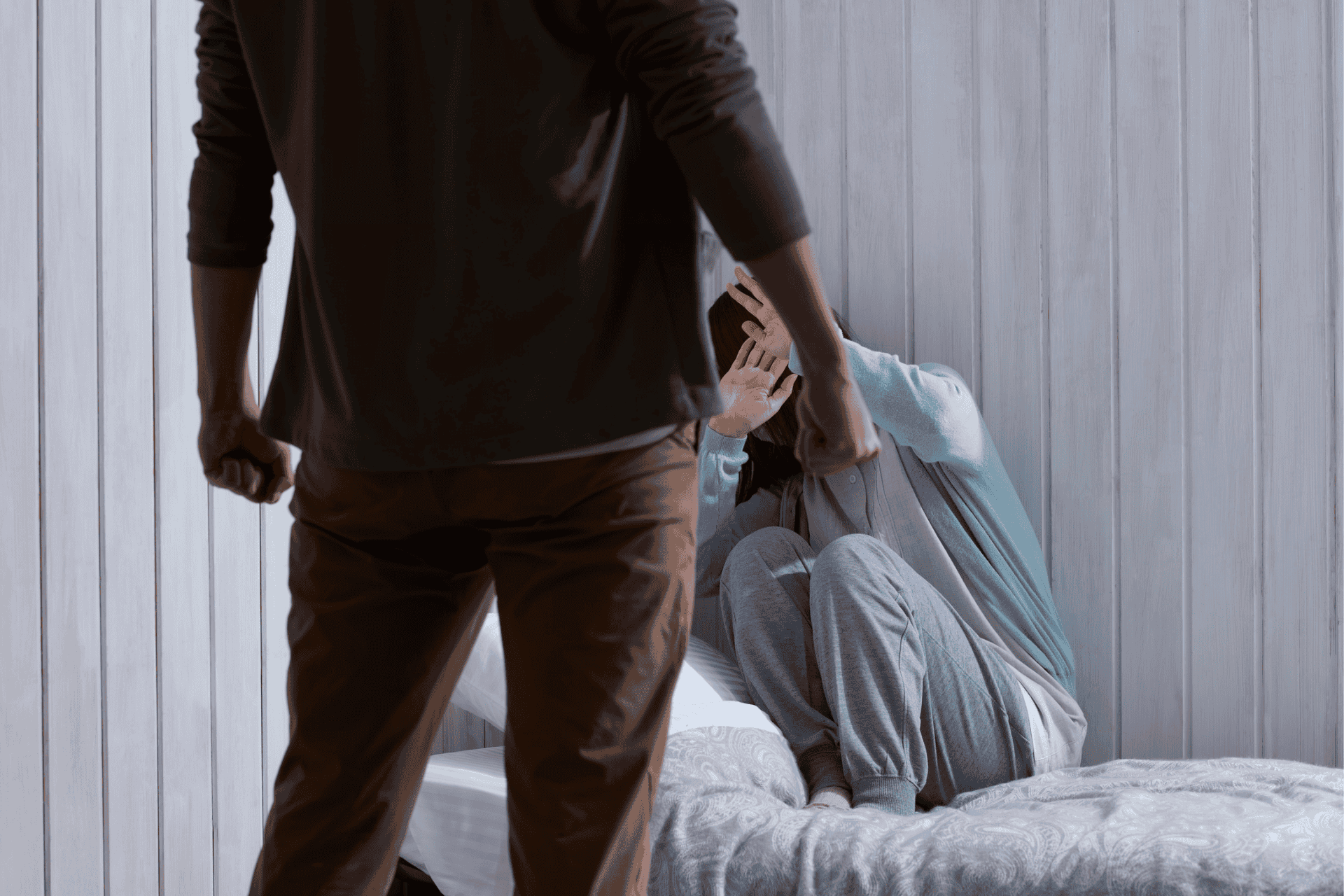 A person stands in the foreground while another individual cringes in a corner, illustrating a domestic conflict.