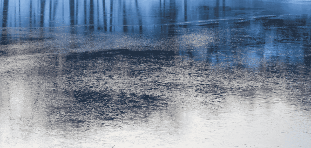 A scenic, blue-toned landscape that reflects an icy pond at Voice of America (VOA) MetroPark with reflections of trees on the frozen surface.