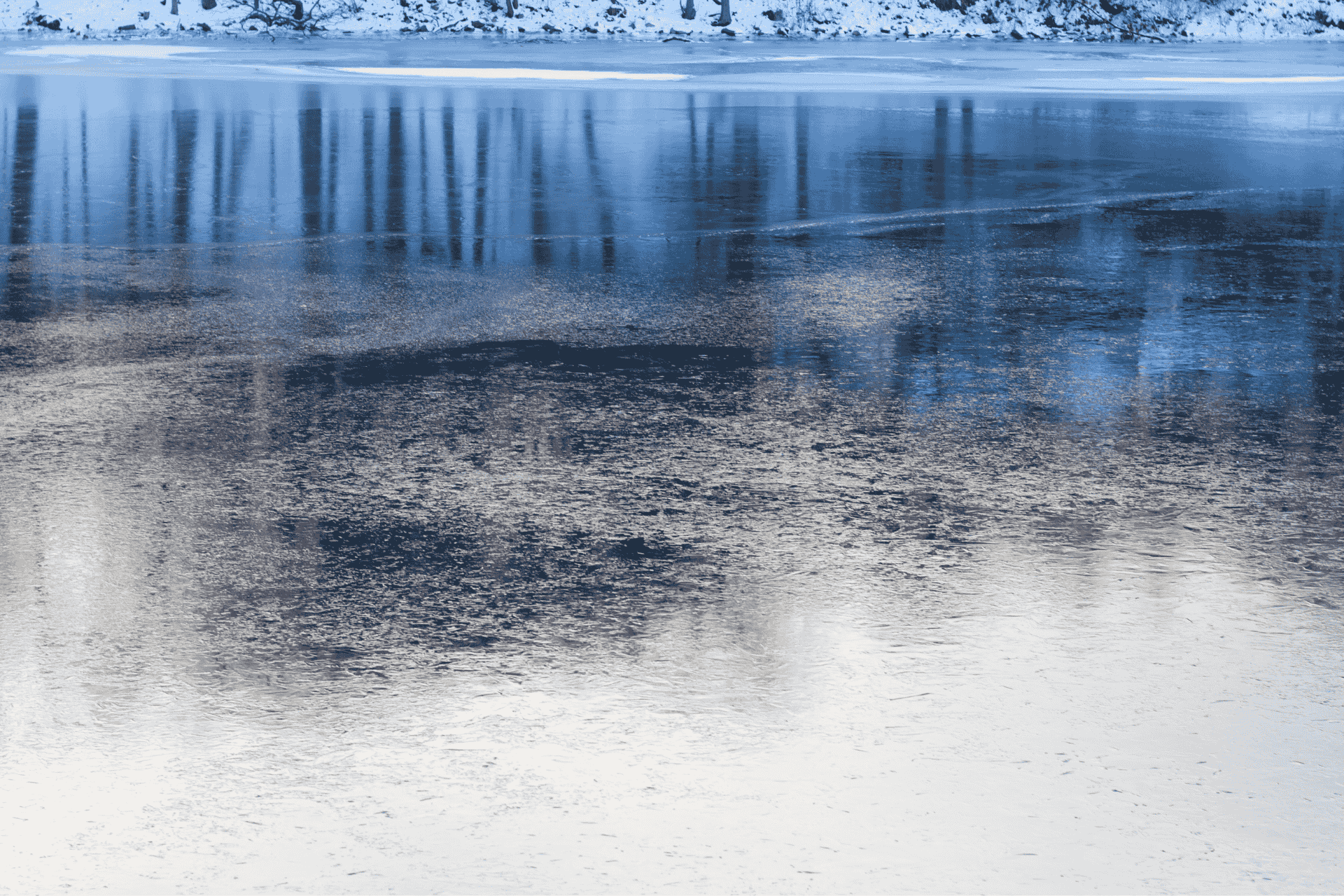 A scenic, blue-toned landscape that reflects an icy pond at Voice of America (VOA) MetroPark with reflections of trees on the frozen surface.