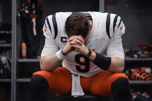 Joe Burrow sits in the locker room with his head down after a game, wearing a Cincinnati Bengals uniform
