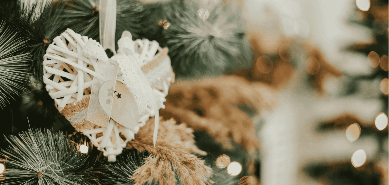 Rustic white woven heart ornament hanging on a Christmas tree branch with warm bokeh lights, symbolizing holiday wishes in Cincinnati.