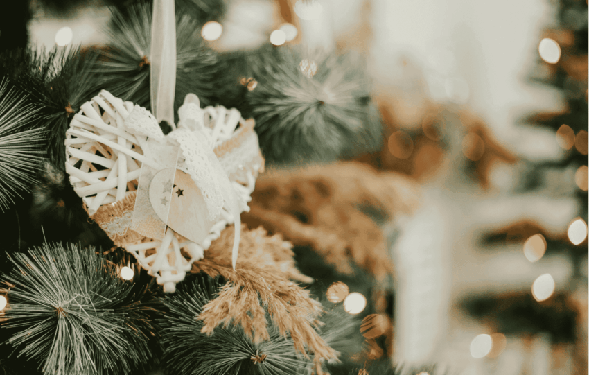 Rustic white woven heart ornament hanging on a Christmas tree branch with warm bokeh lights, symbolizing holiday wishes in Cincinnati.