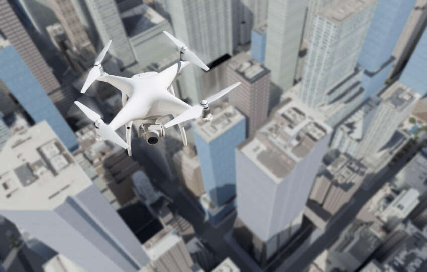 A white quadcopter drone flying high above a dense city skyline of skyscrapers, representing the Drones as First Responders program in Cincinnati.