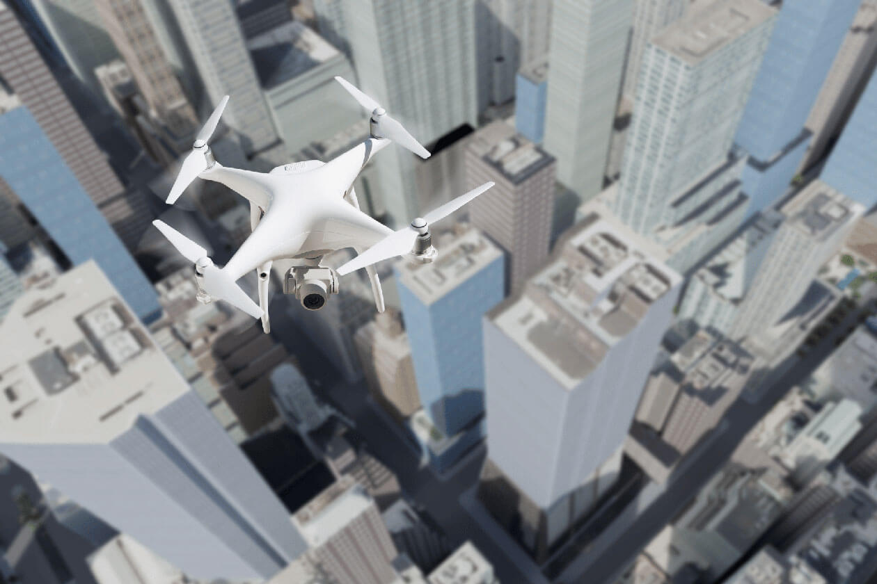 A white quadcopter drone flying high above a dense city skyline of skyscrapers, representing the Drones as First Responders program in Cincinnati.