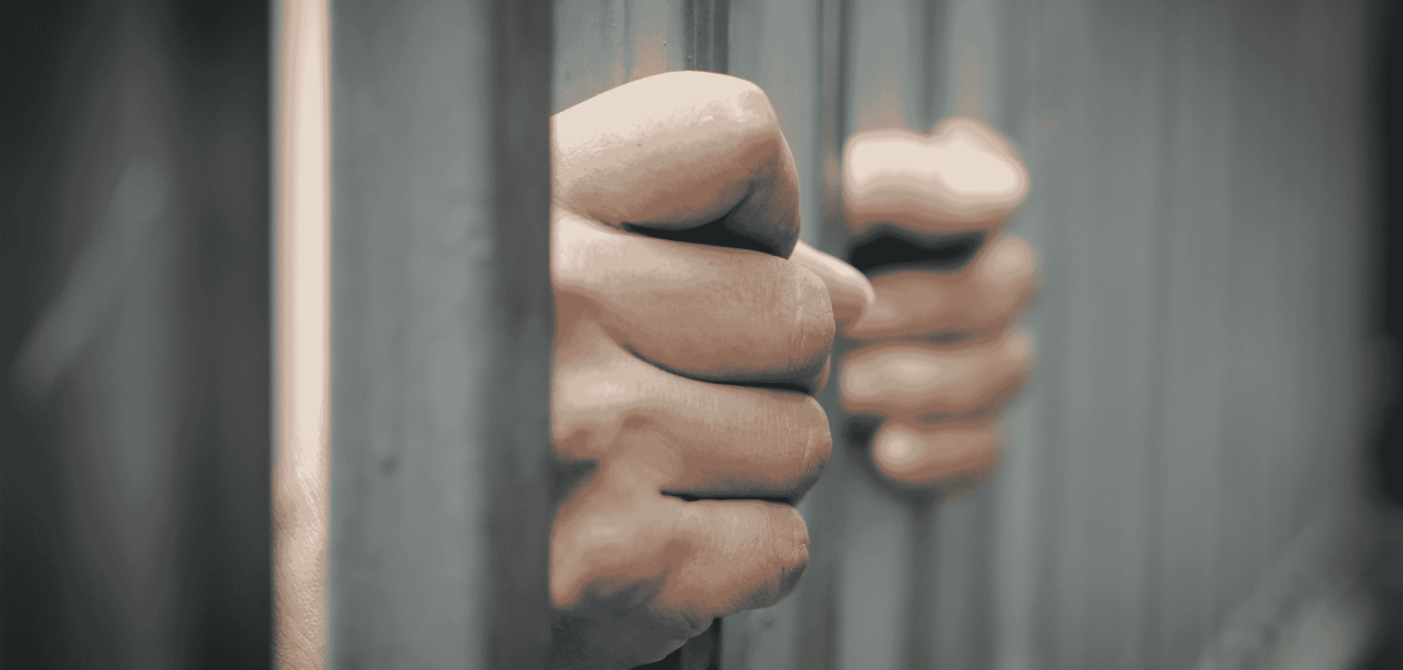 Close-up of hands gripping metal prison bars, representing incarceration and legal consequences.