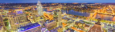High-angle twilight view of the Cincinnati skyline with illuminated skyscrapers, the Great American Tower, and the Ohio River in the background.