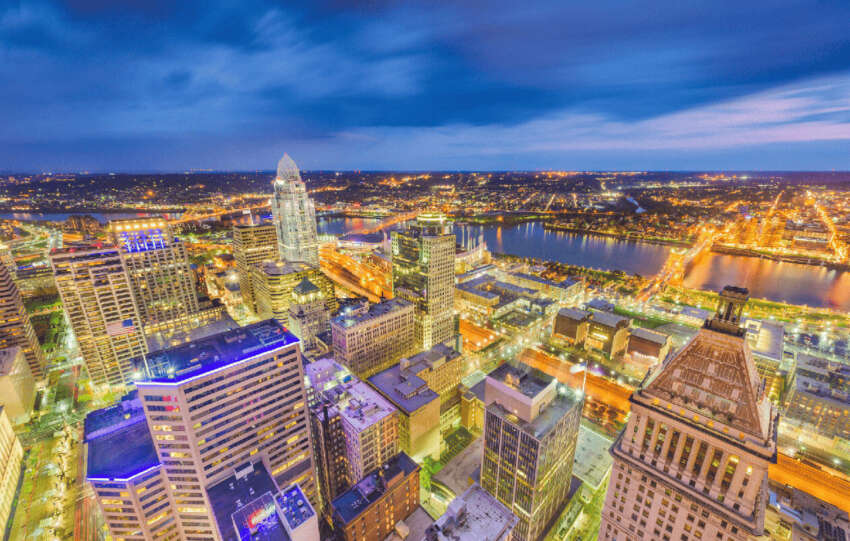 High-angle twilight view of the Cincinnati skyline with illuminated skyscrapers, the Great American Tower, and the Ohio River in the background.