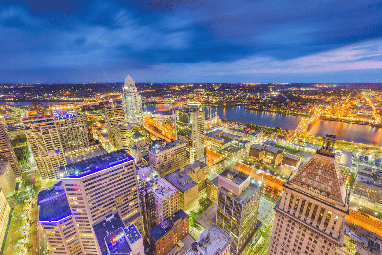 High-angle twilight view of the Cincinnati skyline with illuminated skyscrapers, the Great American Tower, and the Ohio River in the background.