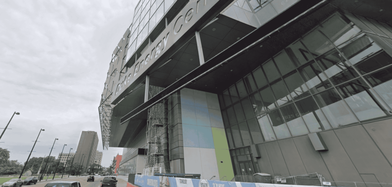 Exterior view of the Duke Energy Convention Center in Cincinnati during ongoing renovations, featuring a modern glass façade and street-level construction barriers.