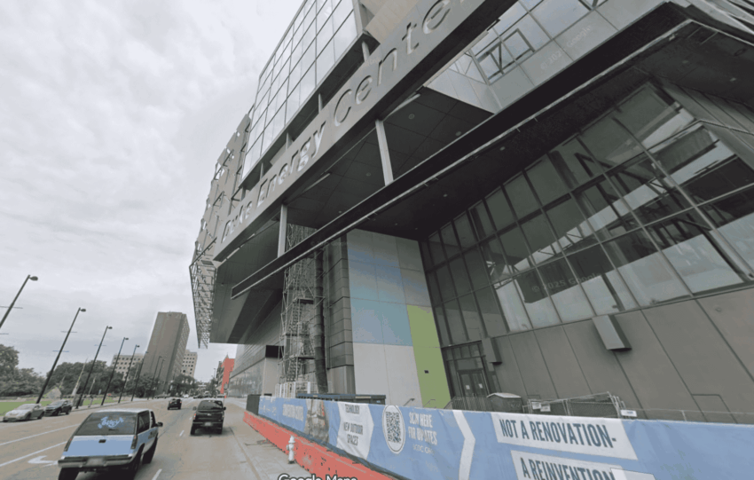 Exterior view of the Duke Energy Convention Center in Cincinnati during ongoing renovations, featuring a modern glass façade and street-level construction barriers.
