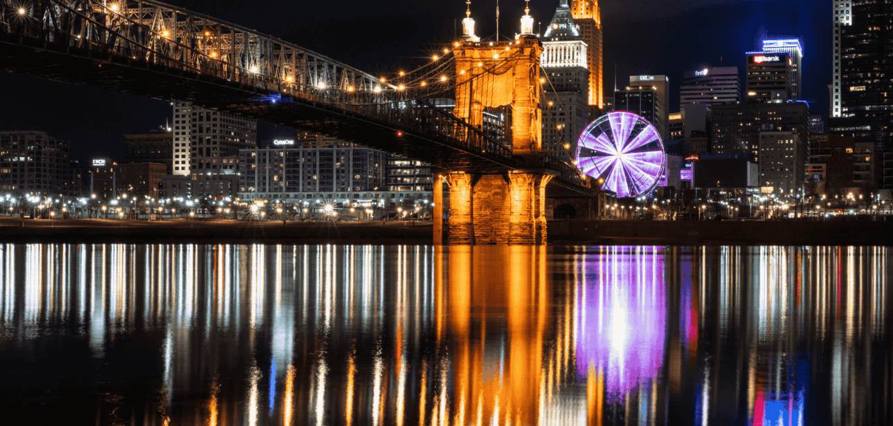 Nighttime view of the Cincinnati skyline and illuminated Roebling Suspension Bridge reflecting on the Ohio River.