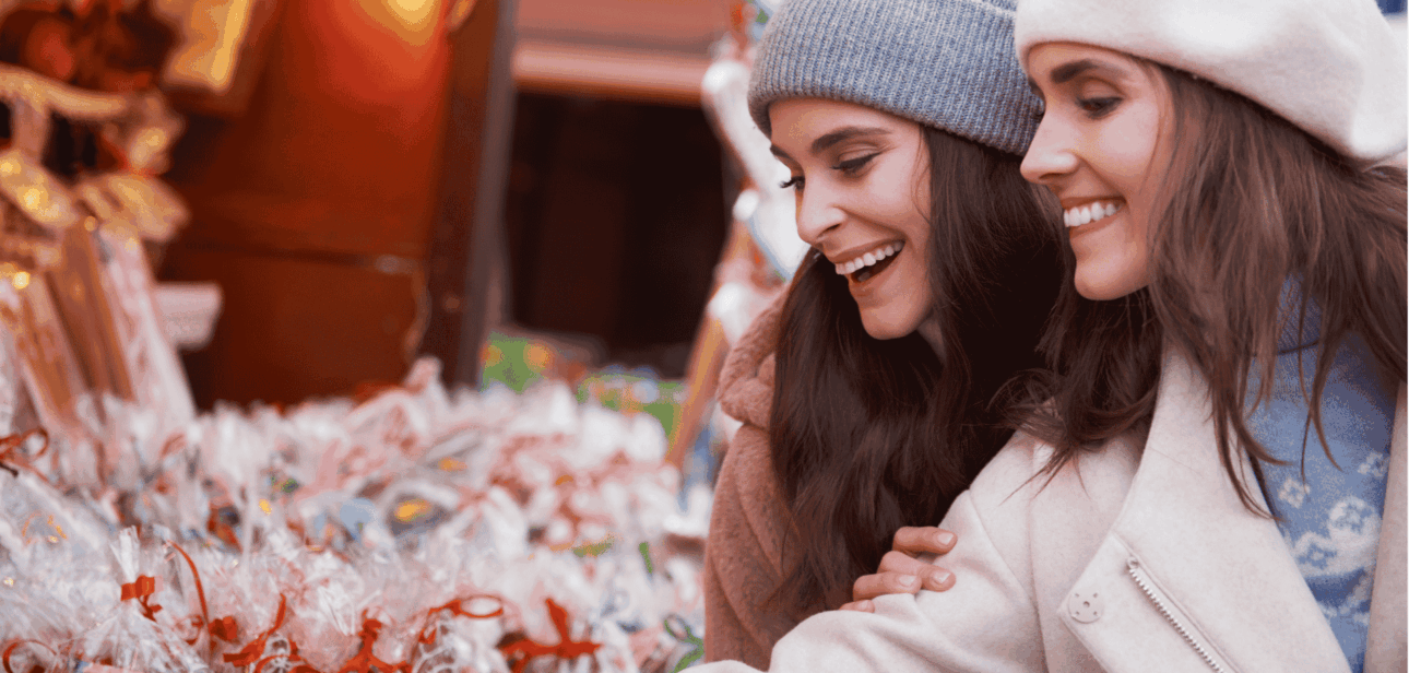 Stock image of two smiling women wearing winter hats and coats browsing a festive outdoor Christmas market in Cincinnati.