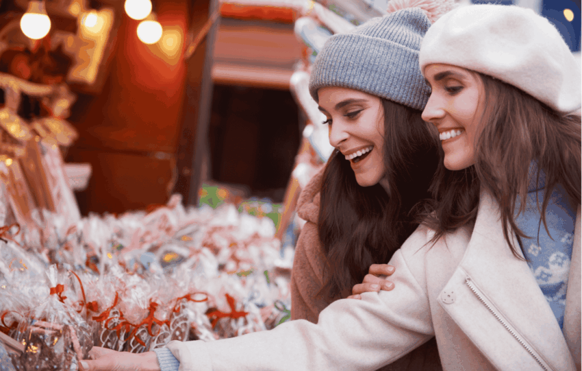 Stock image of two smiling women wearing winter hats and coats browsing a festive outdoor Christmas market in Cincinnati.