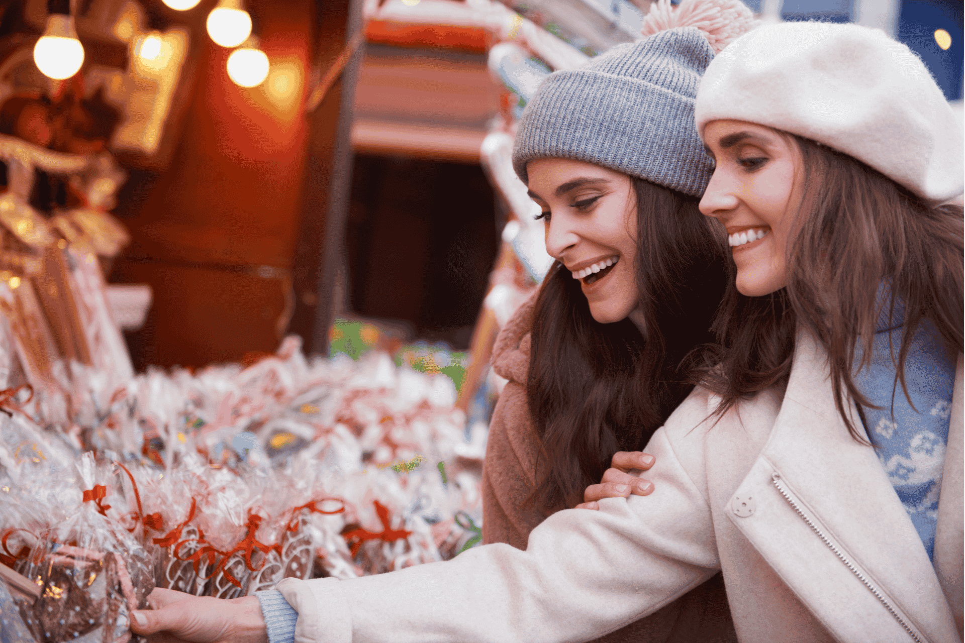 Stock image of two smiling women wearing winter hats and coats browsing a festive outdoor Christmas market in Cincinnati.