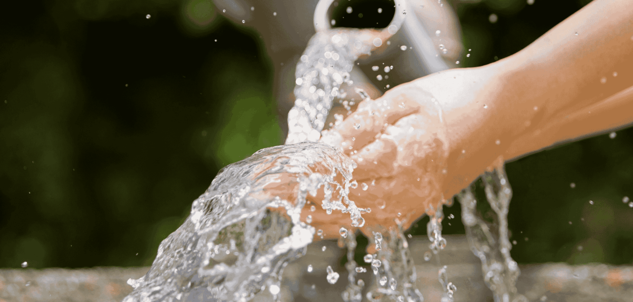 A close-up of hands cupping fresh running water from an outdoor tap, illustrating the surge in water demand.